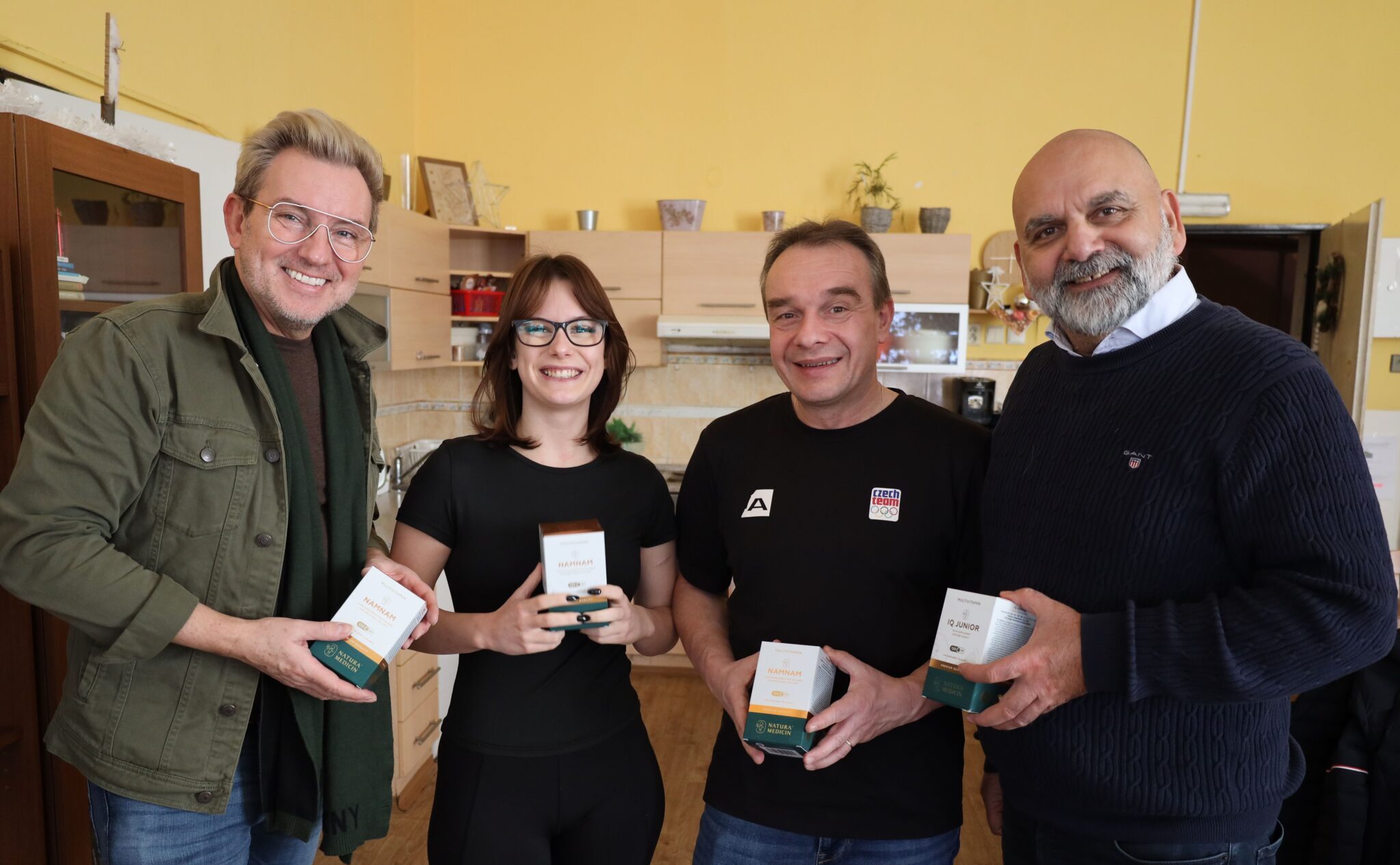 Na obrázku skupina lidí s produkty pro zdraví, představujících odborníky na výživu a zdravotní doplňky s důrazem na prevenci a zdravý životní styl.